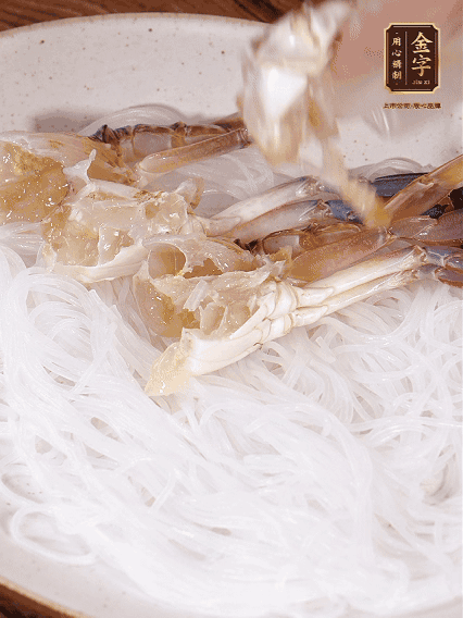 盤底墊上粉絲，擺上梭子蟹、火腿片，撒姜粒，淋上蒸魚豉油、花雕酒調(diào)味腌制15分鐘